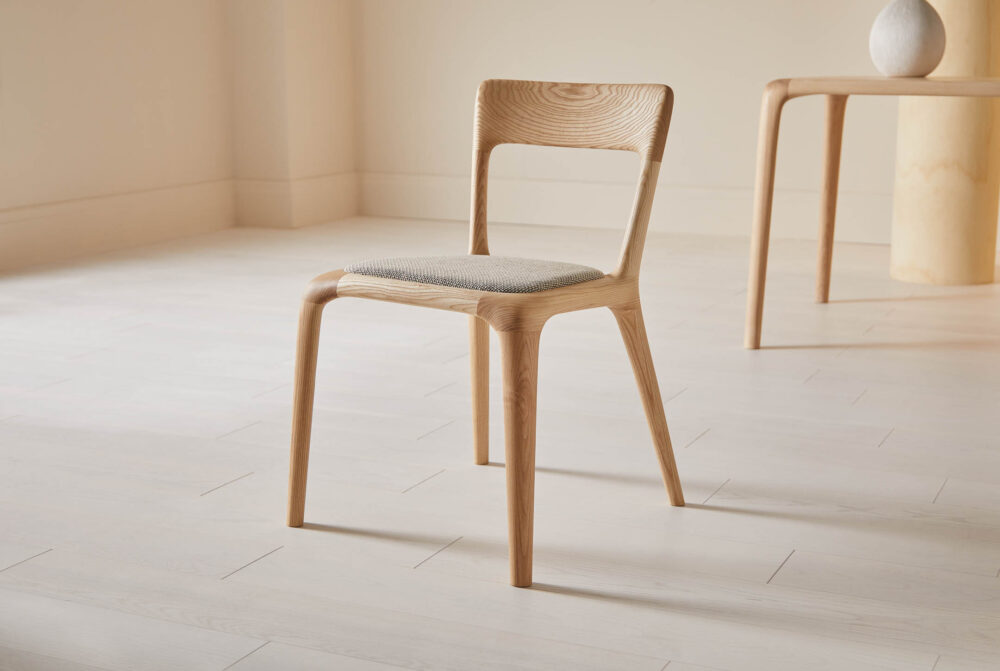 Ash chair with a curved backrest and a grey upholstered seat pad in a minimal room