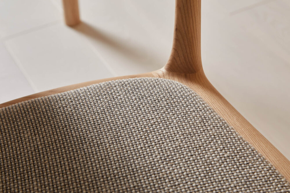 Close-up of grey upholstered seat on ash wood chair, with detailed wood grain texture visible