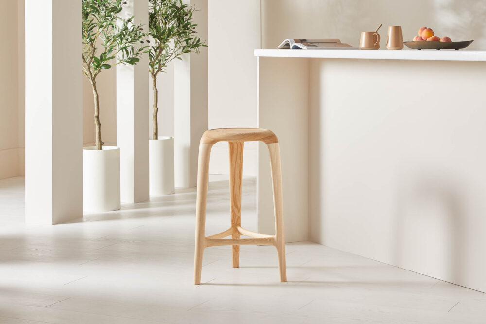 Sculptural ash tripod stool with recessed seat in a minimalist designed space