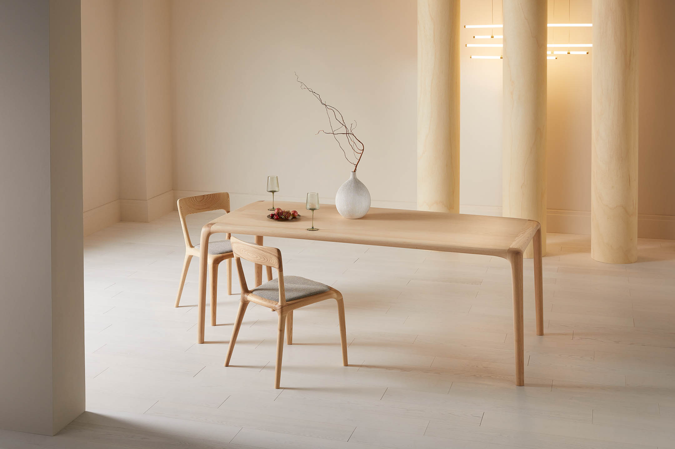 Ash wood dining table with two matching chairs styled with a white vase and glasses in a warm neutral interior